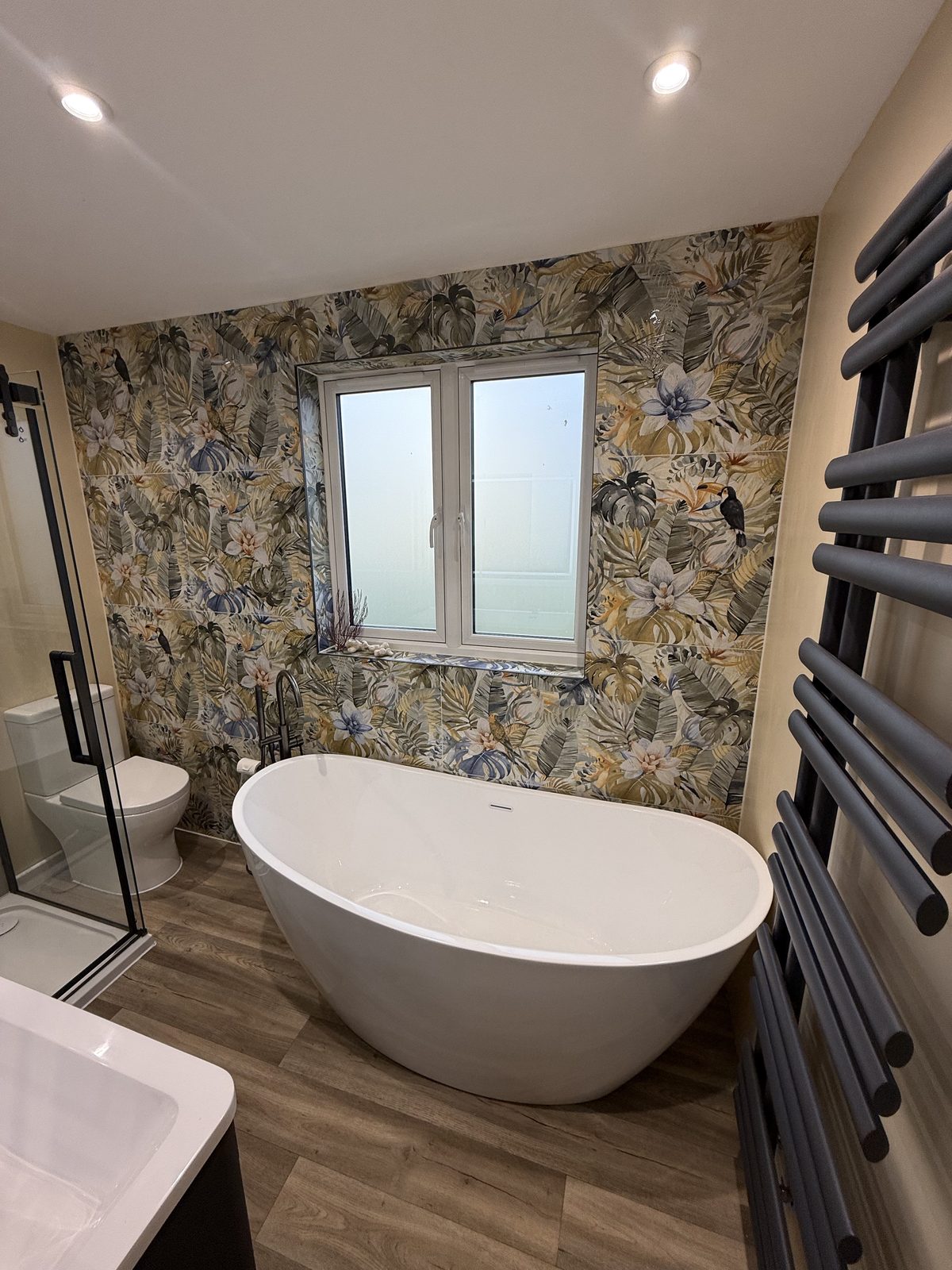 Finished bathroom with freestanding bath, feature wallpaper and black towel radiator